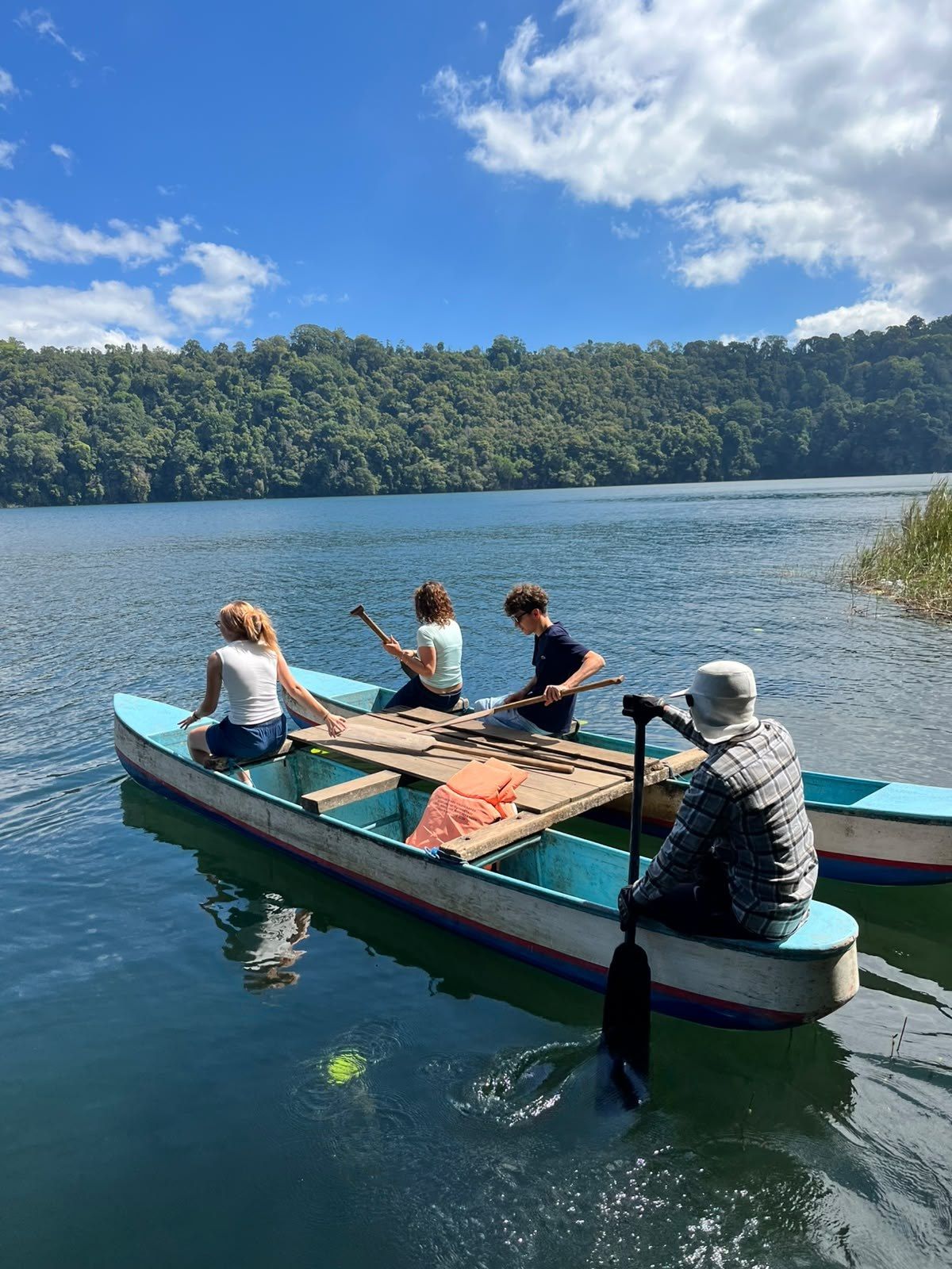 Two wooden canoes crossing Lake Tamblingan under a blue sky