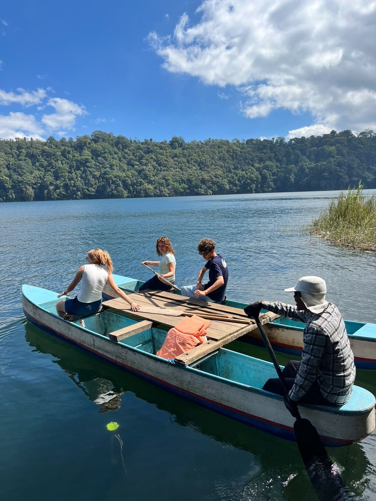Hikers in a wooden canoe on Lake Tamblingan with the forested crater rim behind